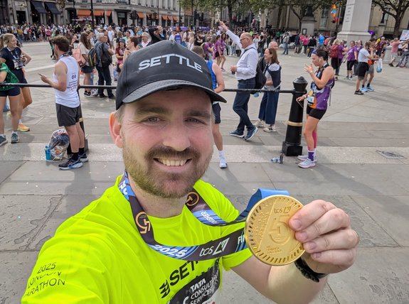 A man in Settle merch is holding up a London marathon medal and celebrating