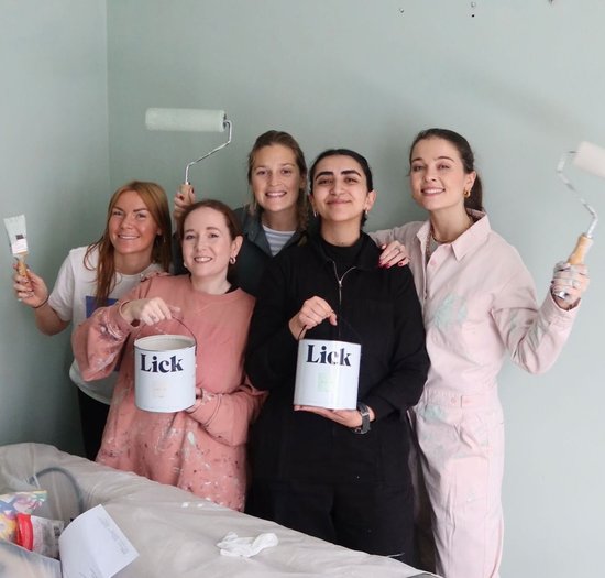 A group of people are smiling wearing painting clothes and holding brushes