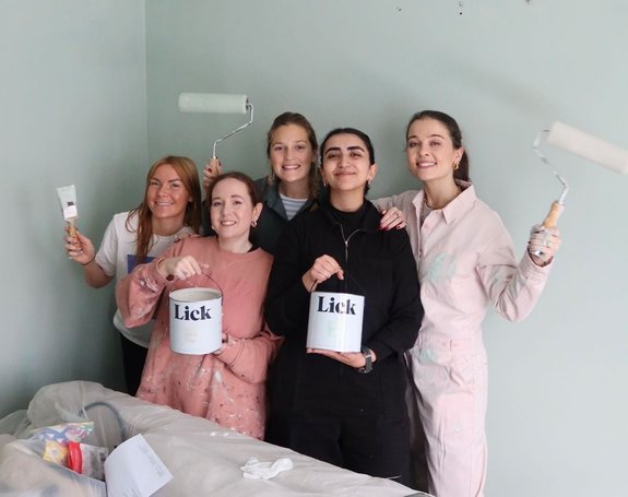 A group of people are smiling wearing painting clothes and holding brushes